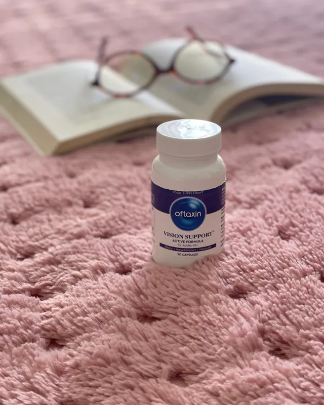 Flacone Oftaxin su una coperta rosa accanto a un libro aperto e un paio di occhiali